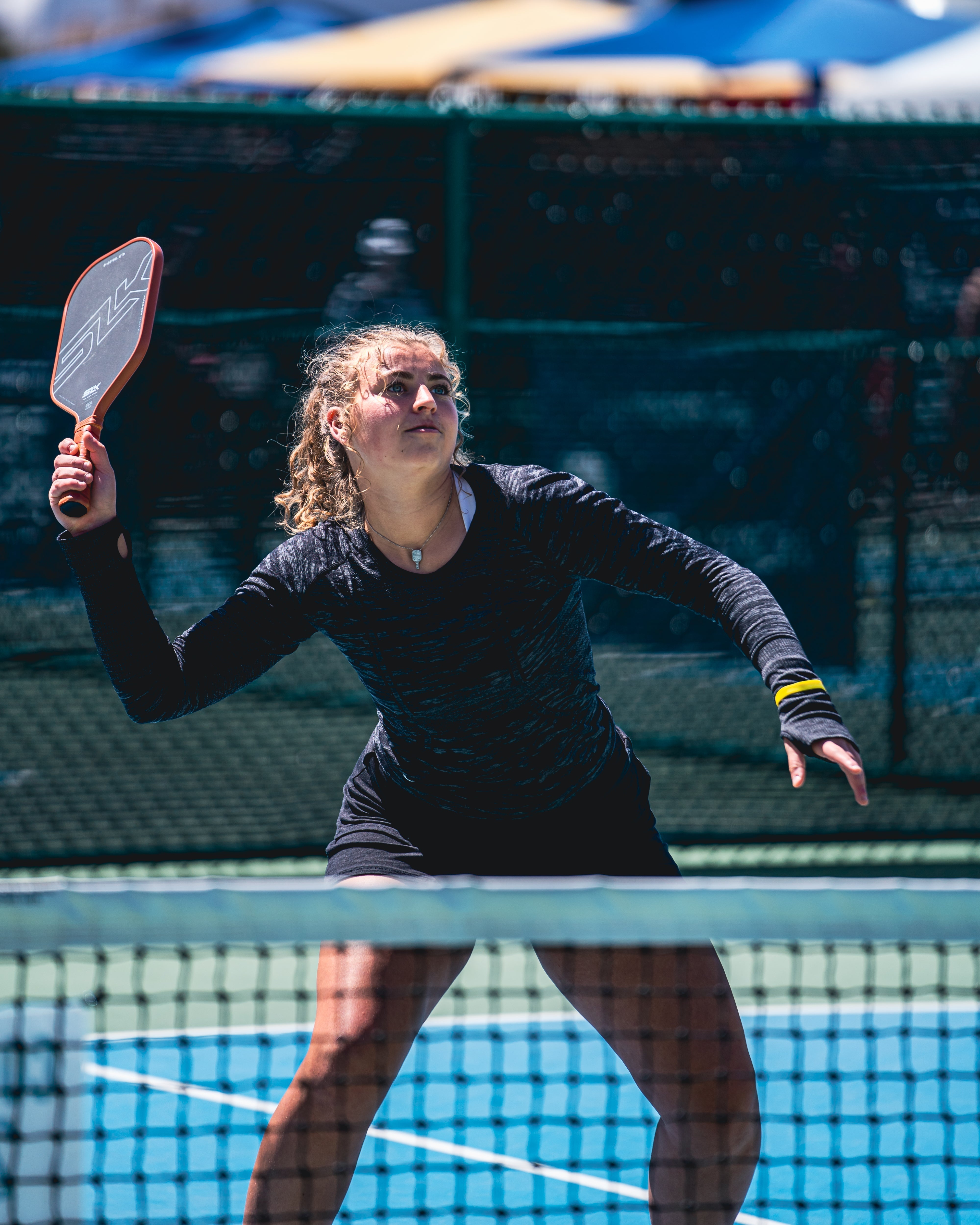 A young female player preparing to hit a pickleball with a paddle on a court.