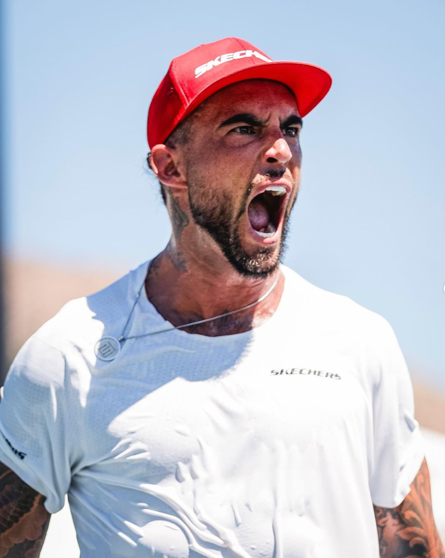 A man celebrating passionately in a white shirt and red cap, likely a player from the tournament.