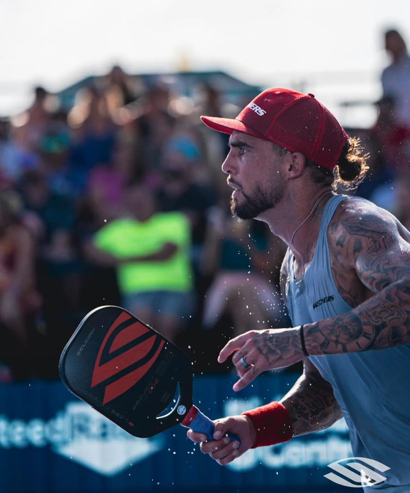 Pickleball player lunging to hit with a Selkirk paddle during a crowded outdoor match