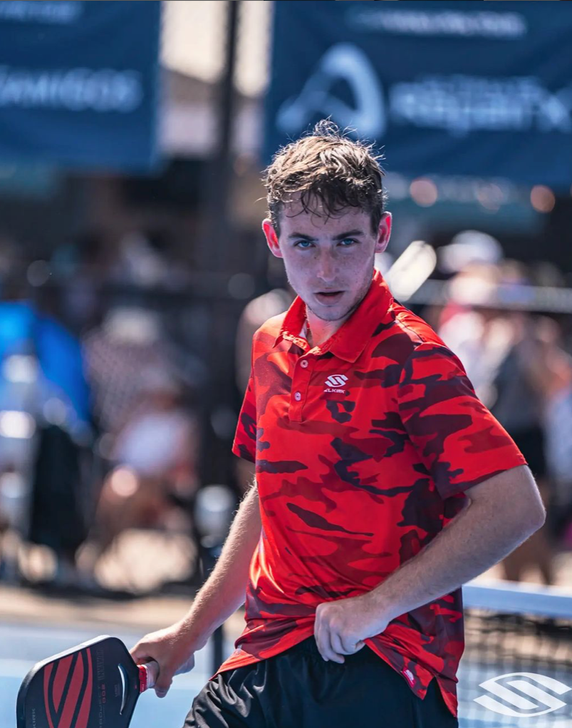 Young male pickleball player in red camo shirt, focused during a match.