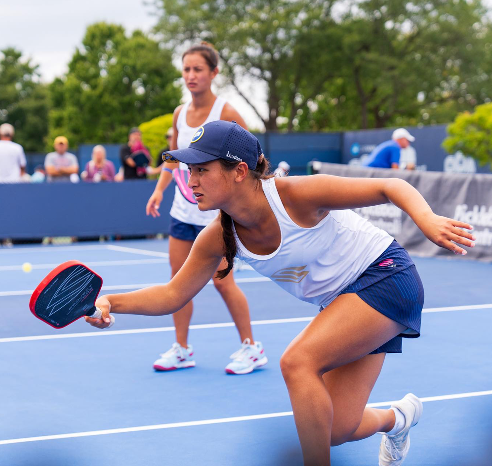 Two female pickleball players on court, one reaching for a shot.