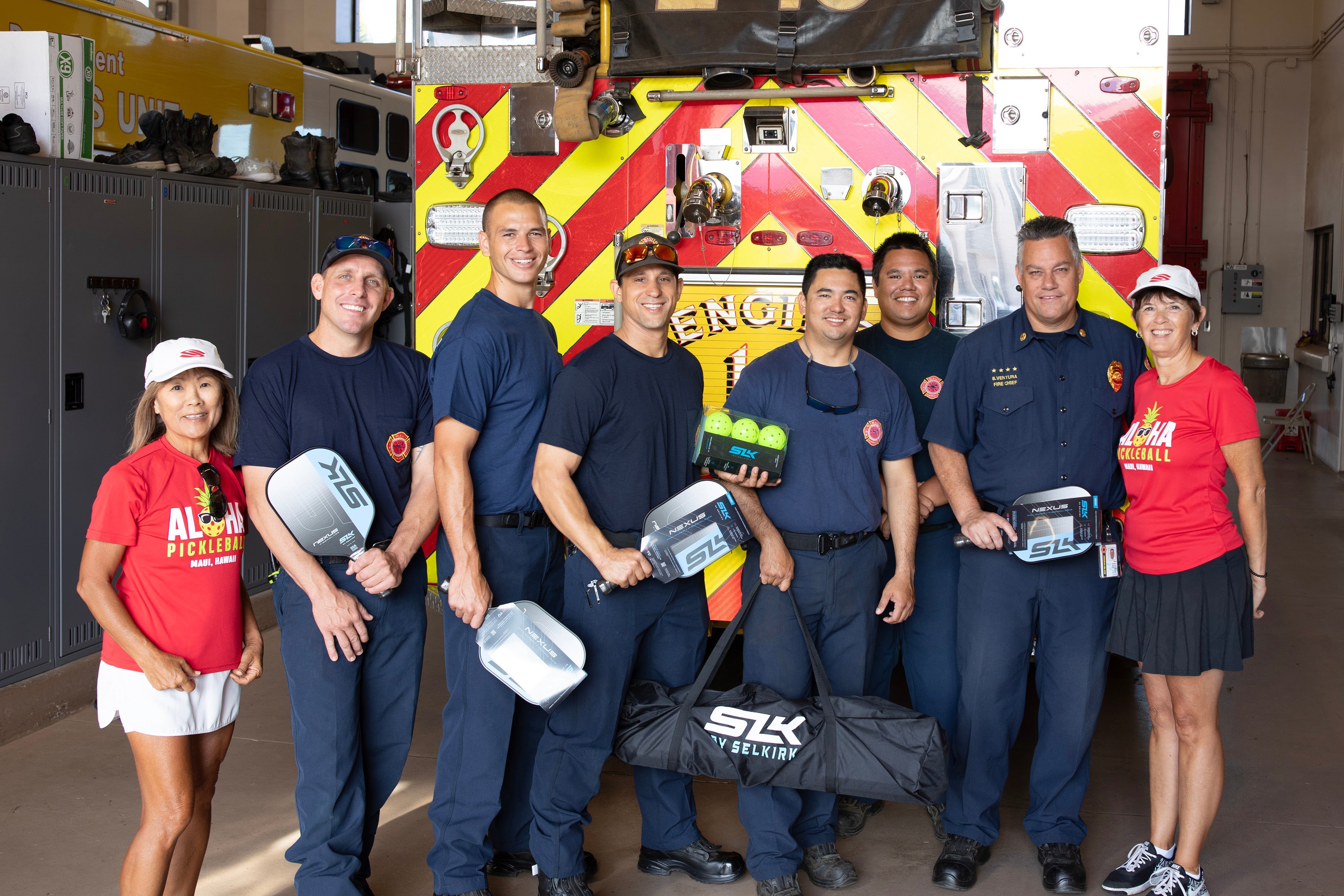 Firefighters holding pickleball paddles and balls in front of a fire truck