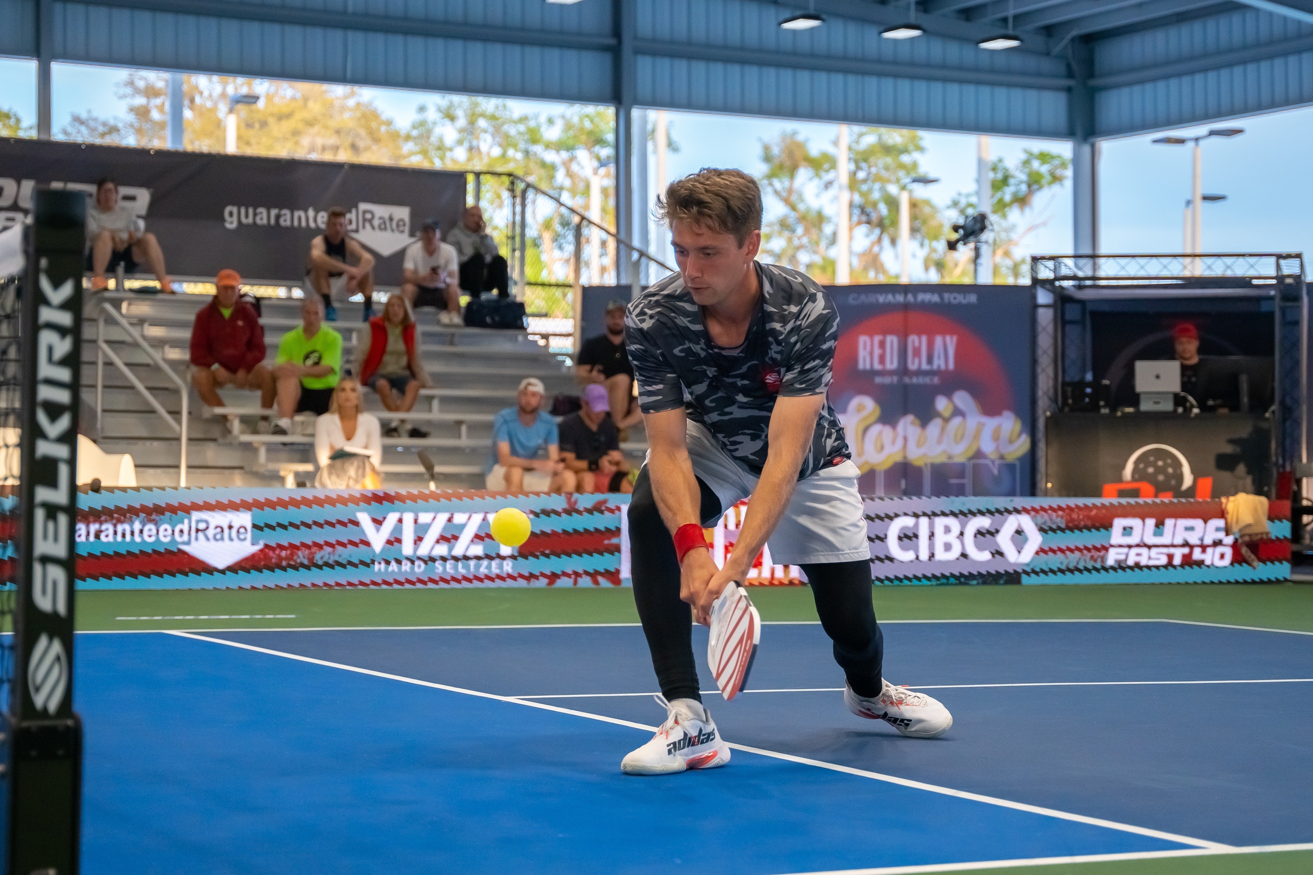 A player in a patterned shirt prepares to hit a ball on a blue court during a tournament.