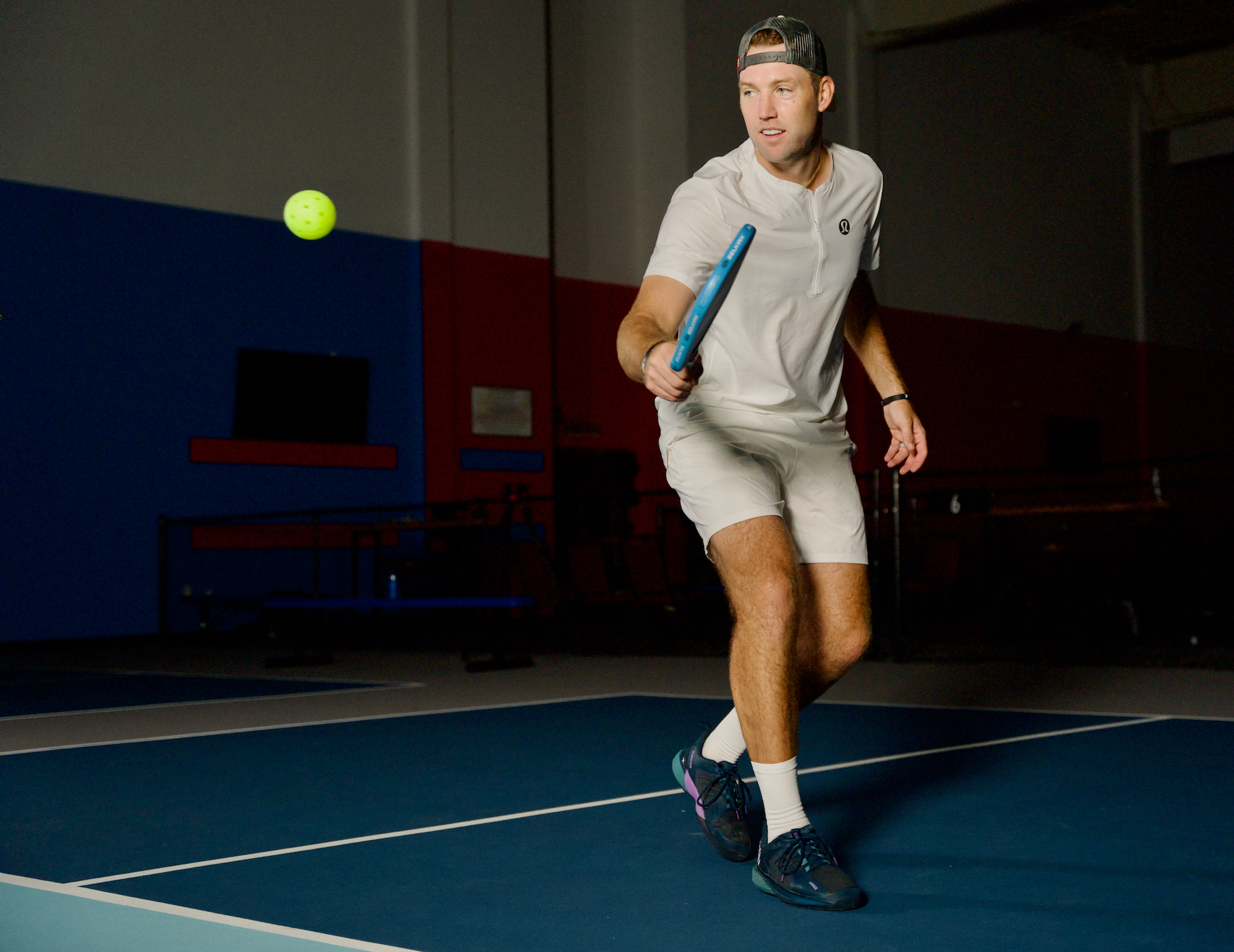 Jack Sock preparing to hit a pickleball with a paddle on a court