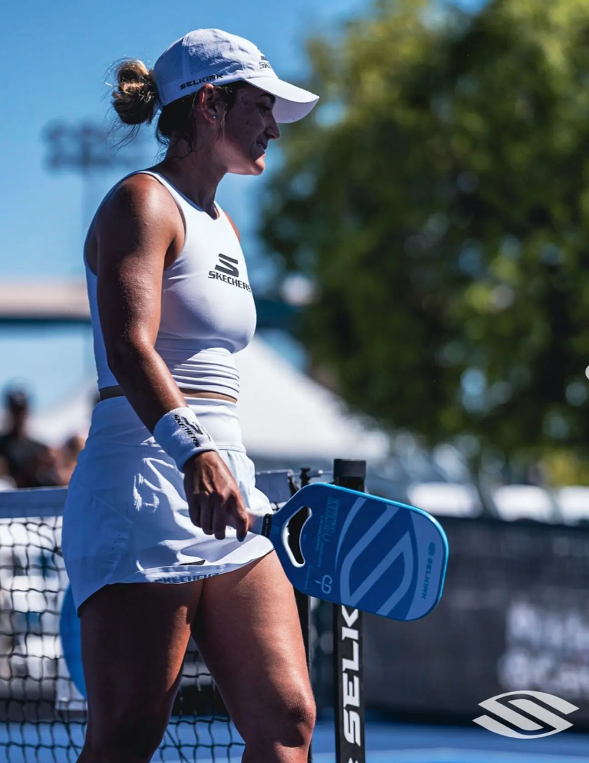 A female pickleball player holding a paddle, standing near the net at a tournament.