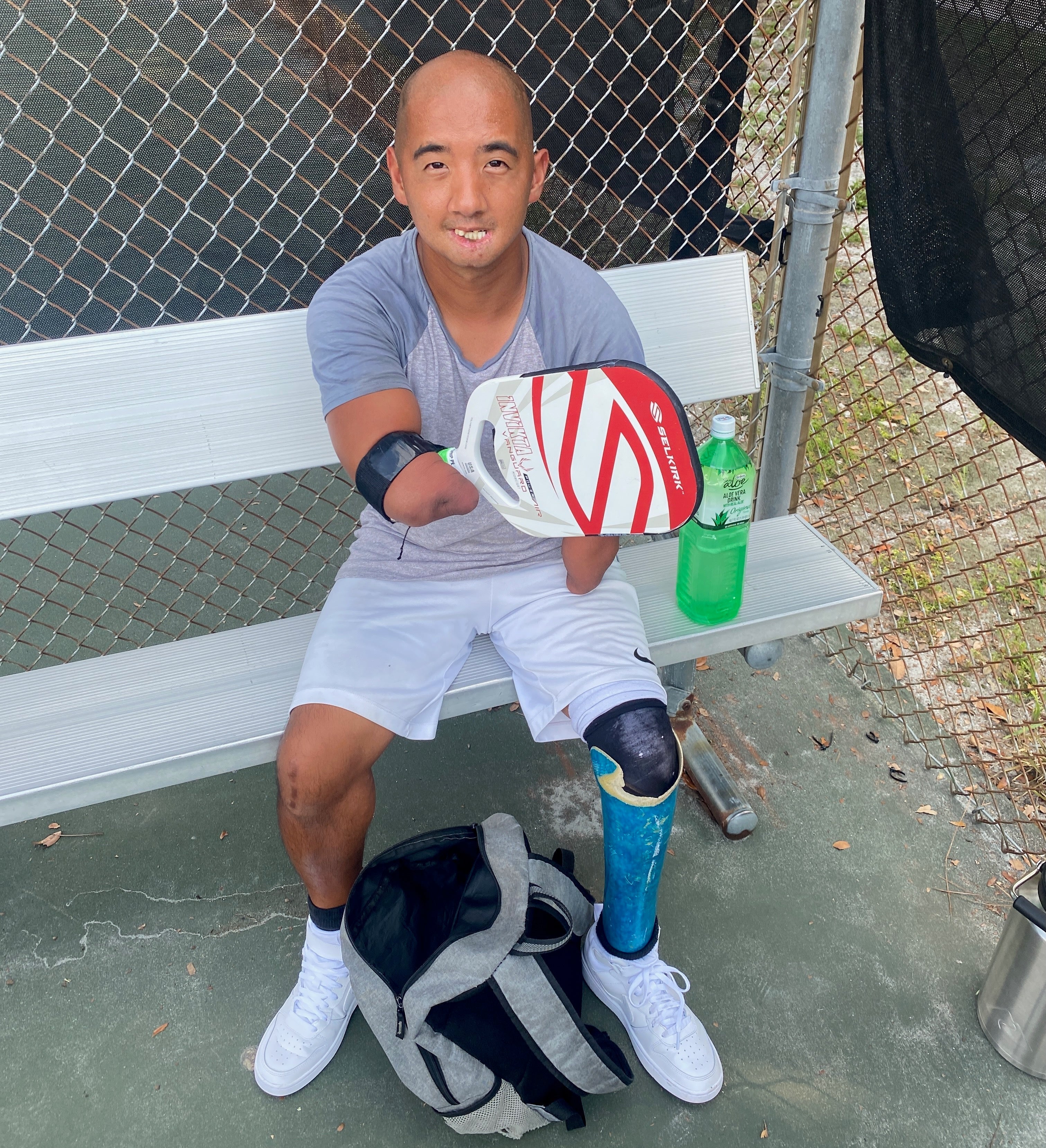 Petey Bruce sitting on a bench with a pickleball paddle and a water bottle, showcasing his adaptive equipment.