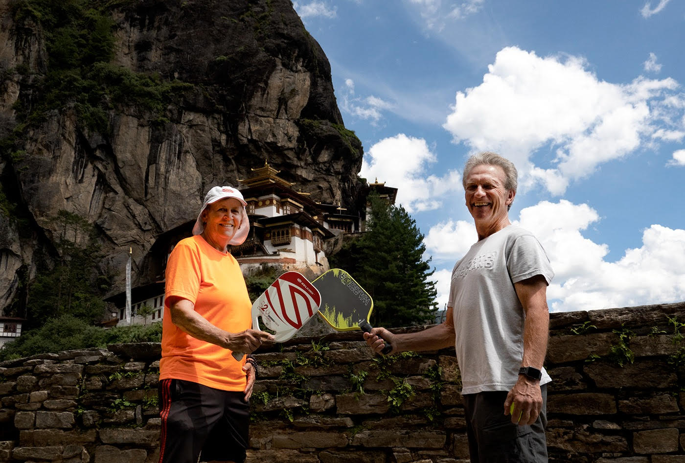 Two pickleball players holding paddles in front of a monastery in Bhutan