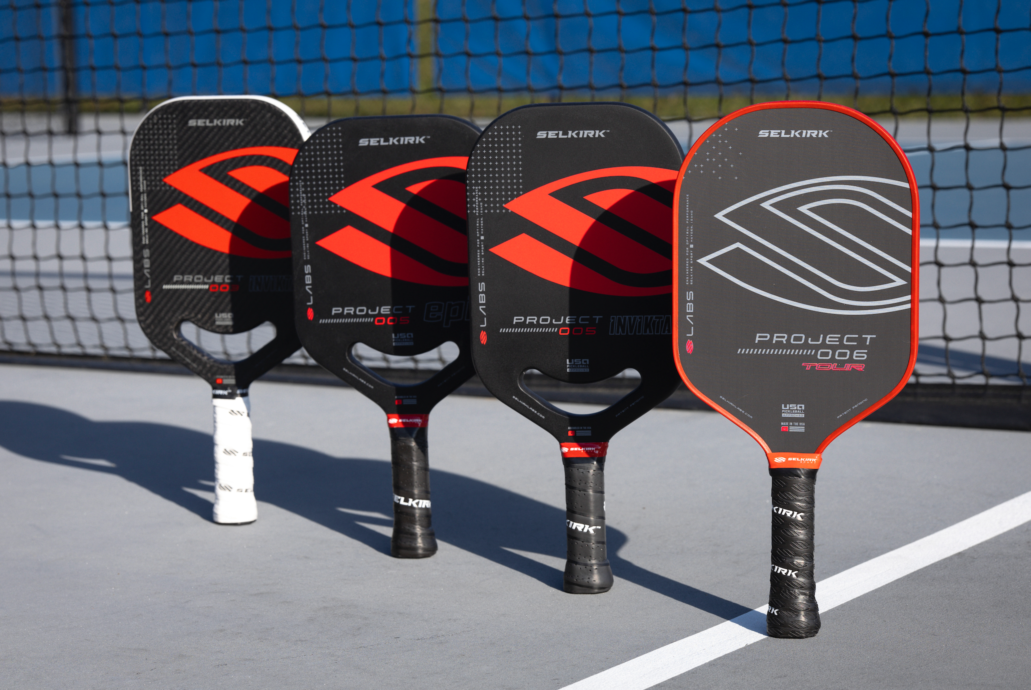 Four Selkirk LABS pickleball paddles lined up on a court, showcasing different designs and colors.