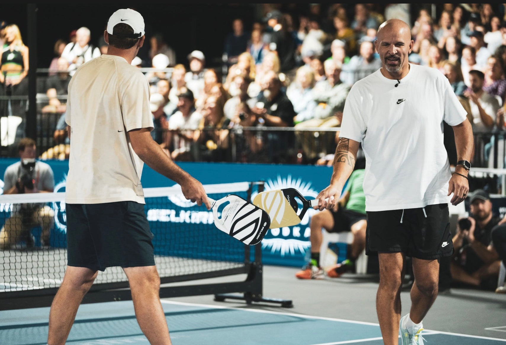 Two players on a pickleball court exchanging Selkirk paddles during the Celebrity Pickleball Showdown.