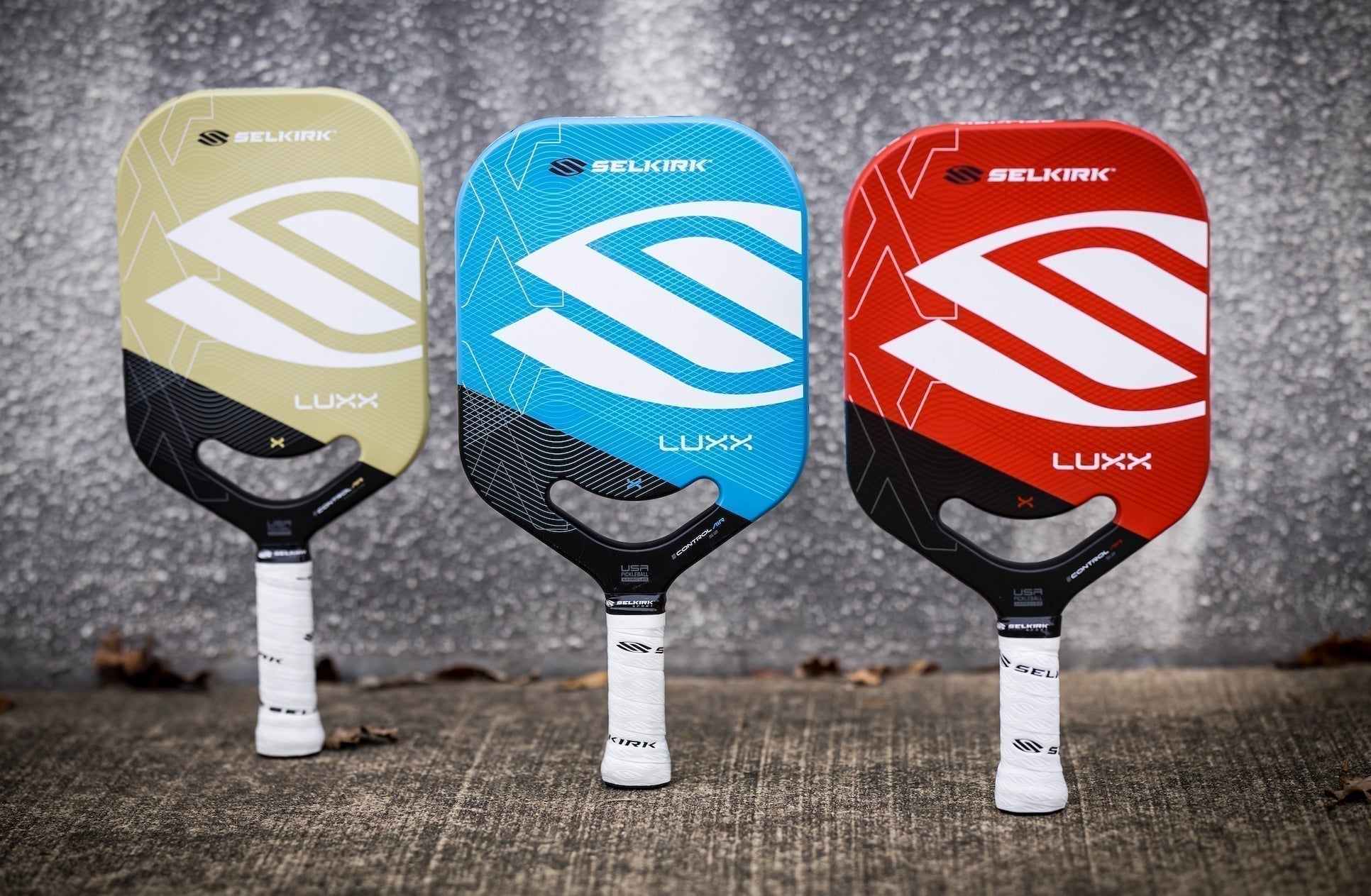 Three Selkirk pickleball paddles in different colors: beige, blue, and red, showcasing their designs.
