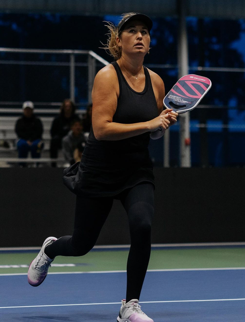 A female pickleball player in motion on the court, holding a paddle.