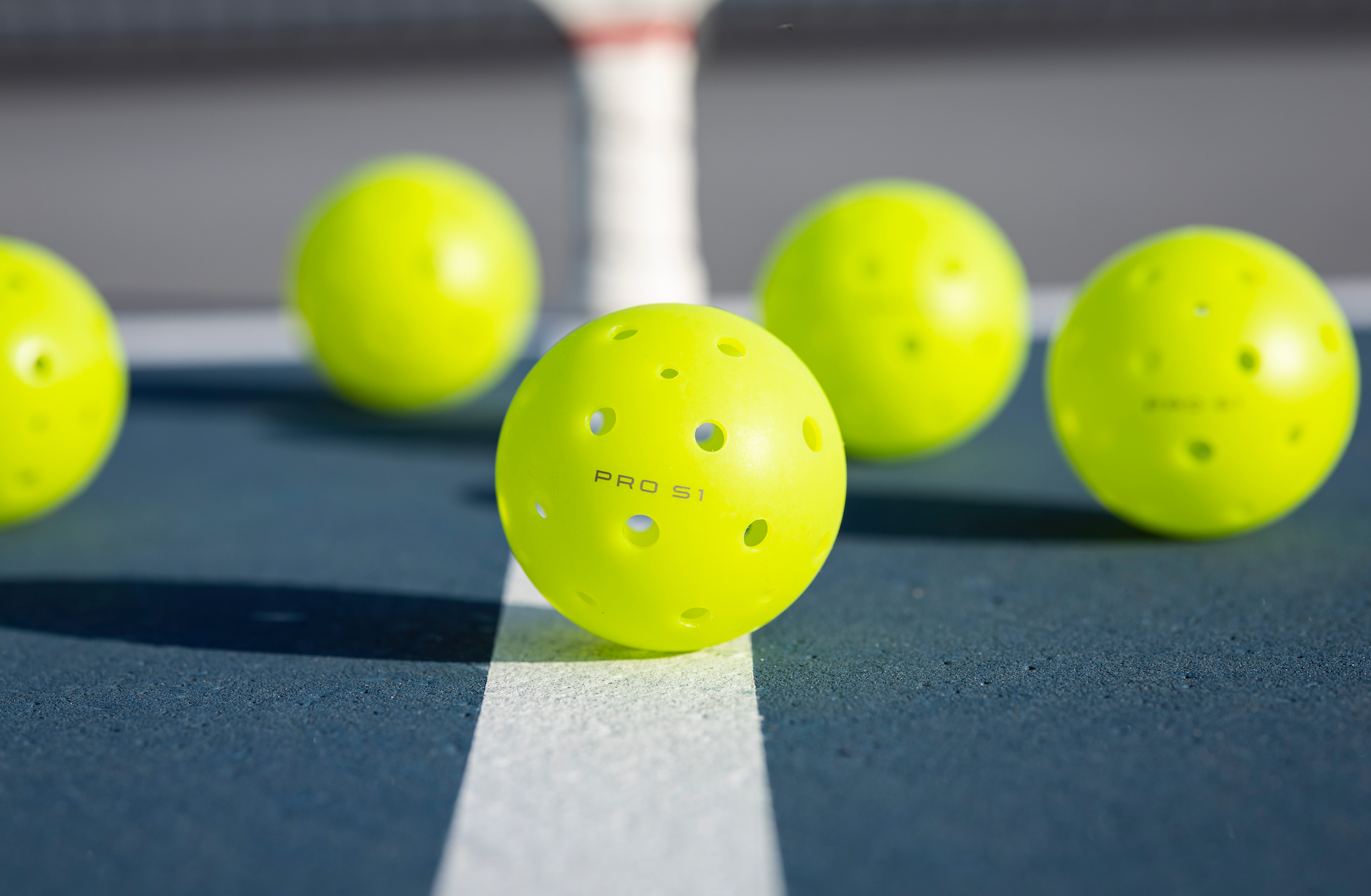 Five bright yellow Pro S1 pickleball balls on a court surface