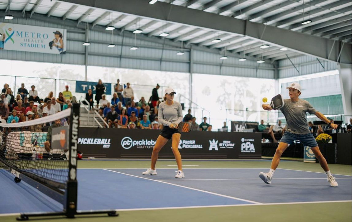 Mixed doubles pickleball players volleying at the net during an indoor tournament with crowd and Selkirk-branded net
