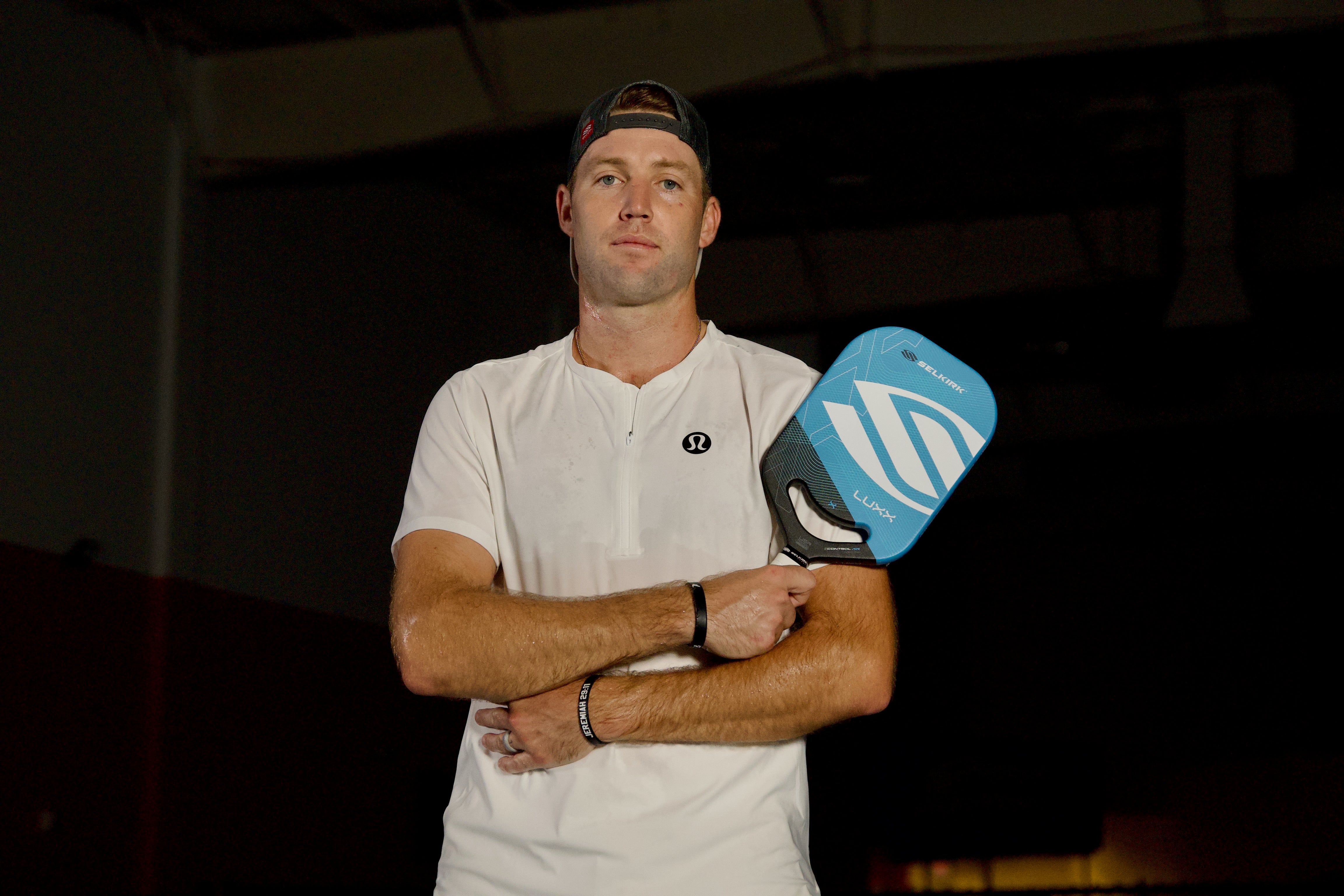 Jack Sock holding a Luxx Control Air pickleball paddle, wearing a white shirt