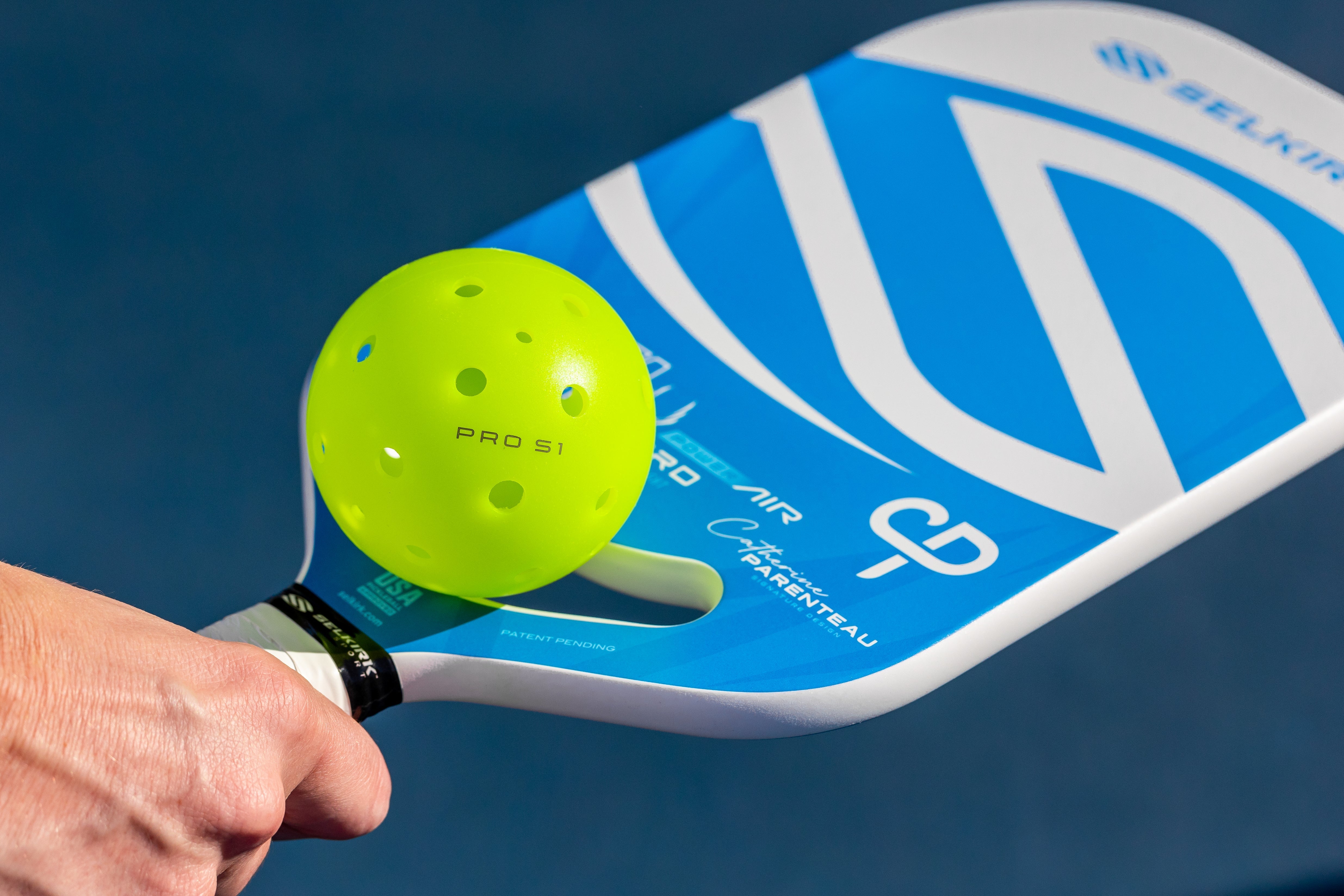 A hand holding a paddle with a bright green Pro S1 pickleball on it