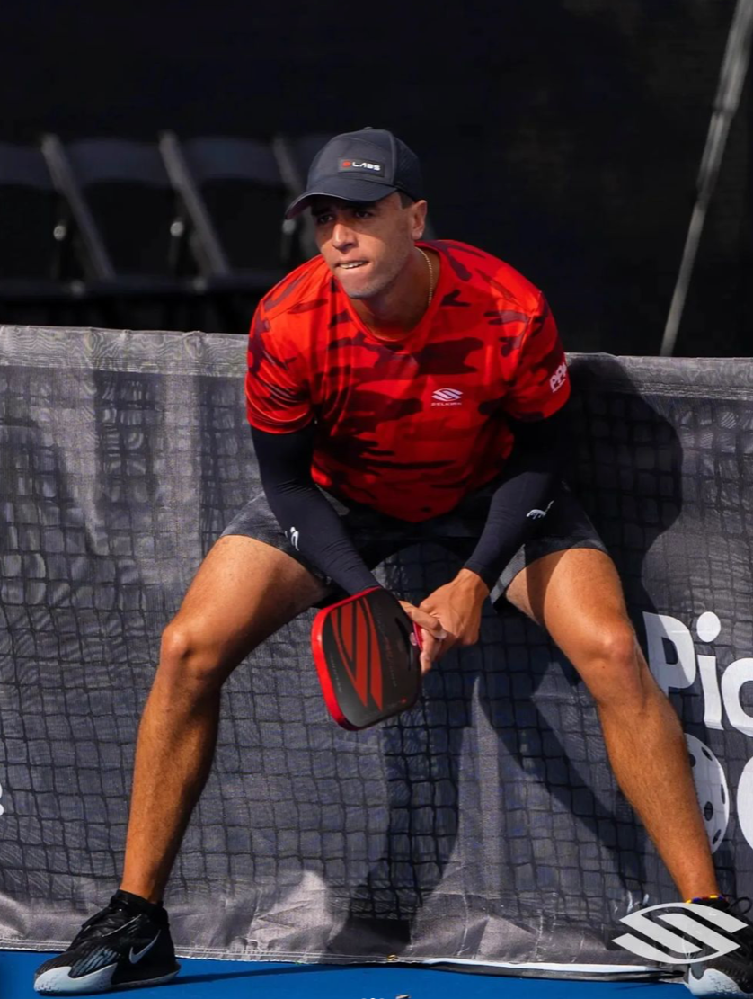A pickleball player in a red shirt preparing to return a shot during a match.
