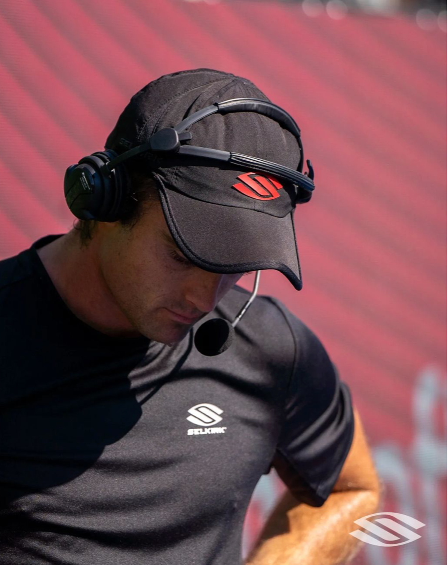 Man wearing a headset, looking down, with a logo on his shirt