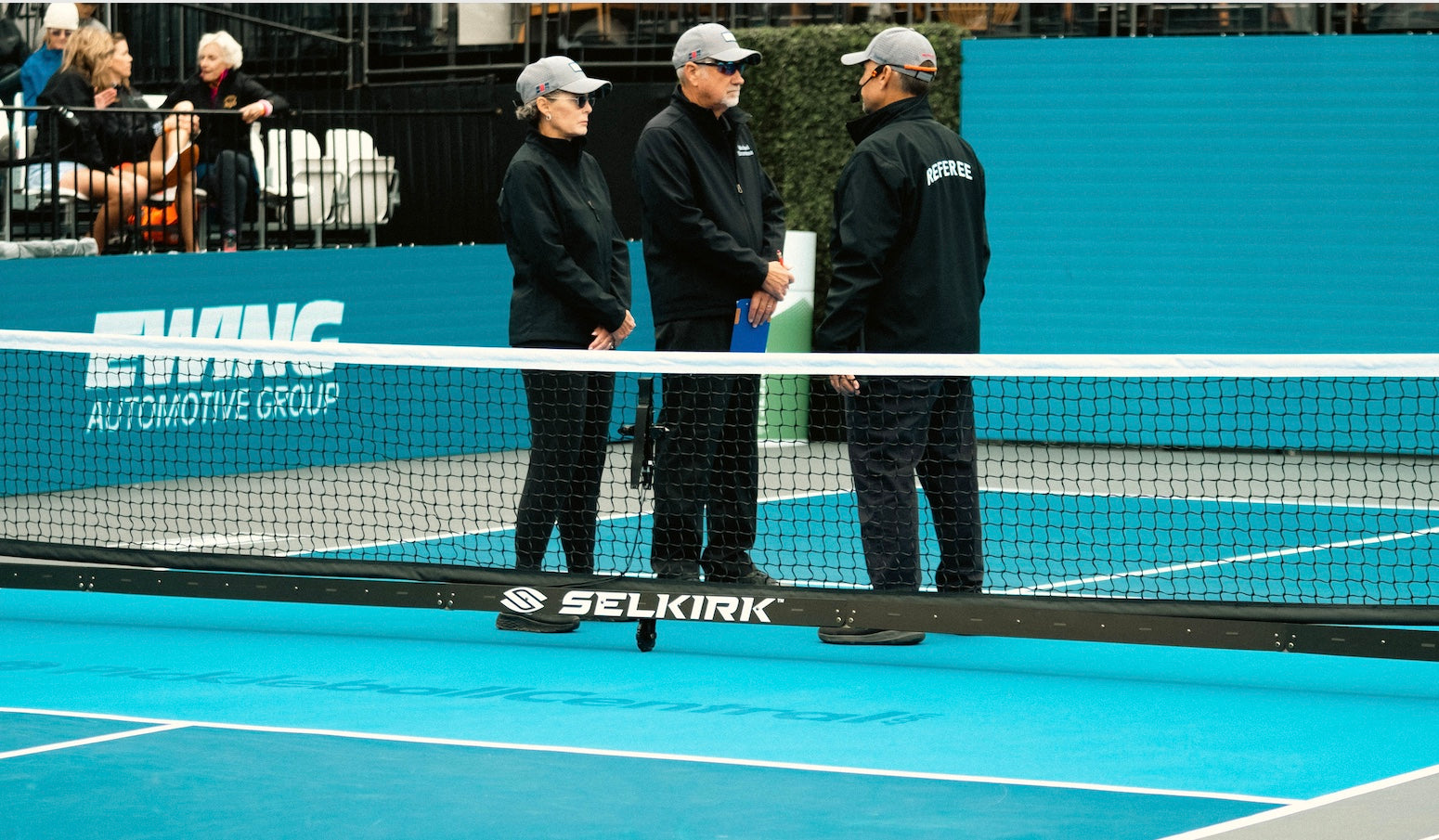 Three officials discussing near a pickleball net on a court