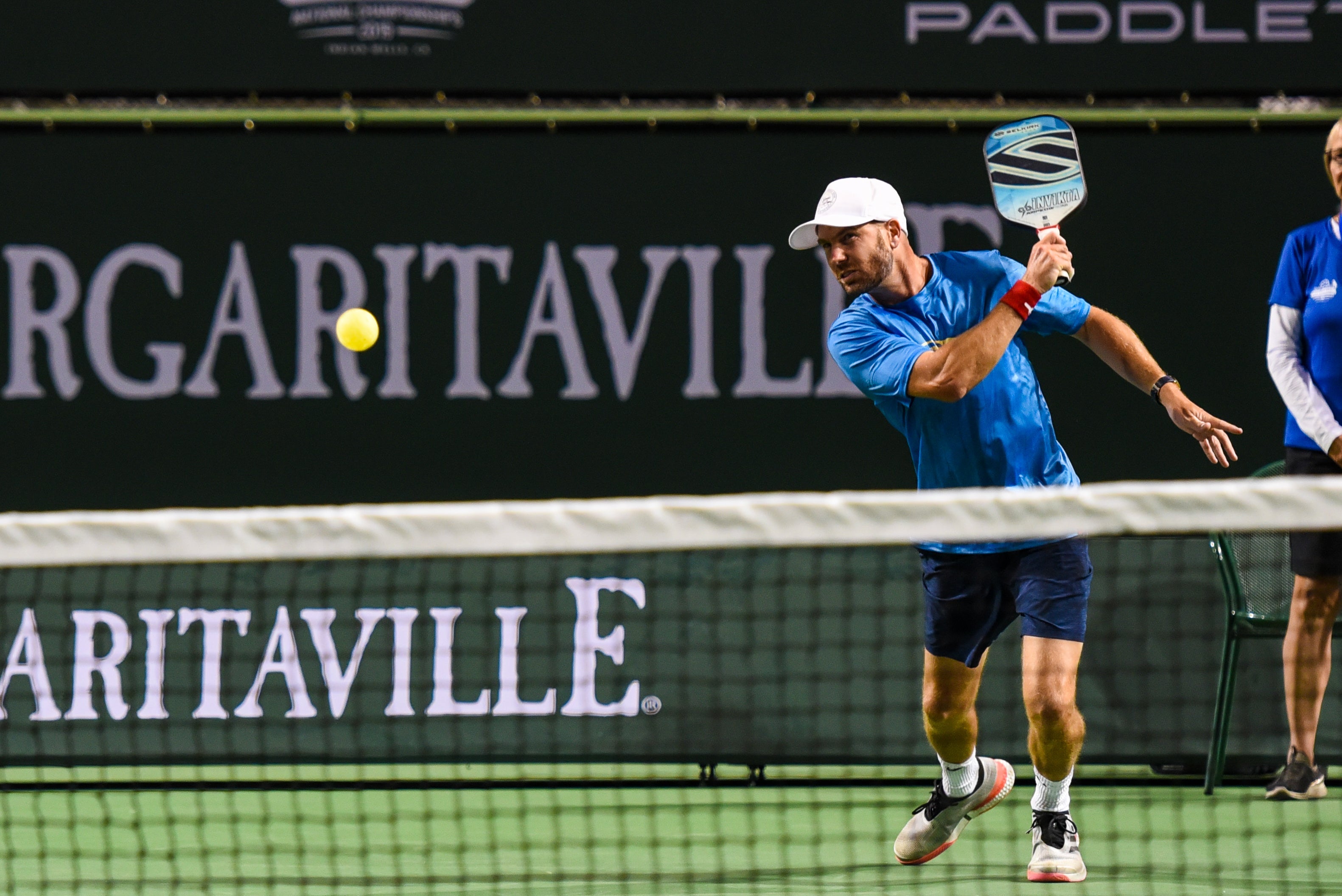 A player in a blue shirt hitting a pickleball with a paddle, focused on the ball.