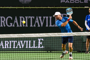A player in a blue shirt hitting a pickleball with a paddle, focused on the ball.