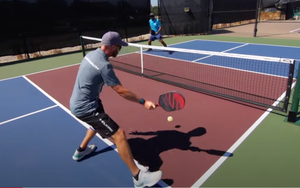 A player hitting a pickleball with a paddle while another player stands ready at the net.