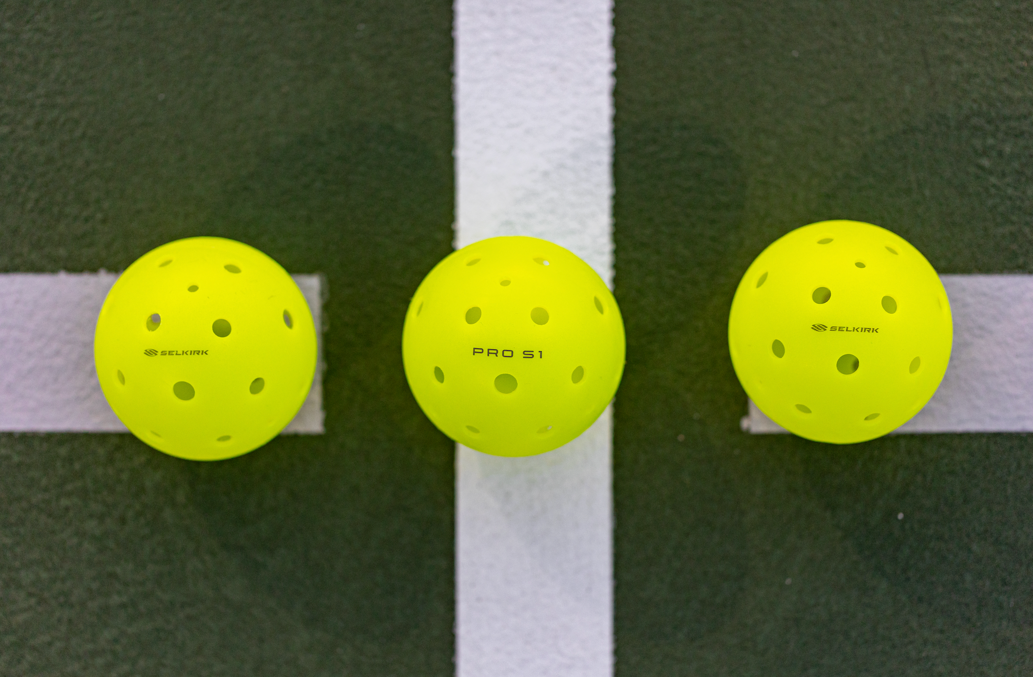 Three yellow Pro S1 pickleballs on a court surface