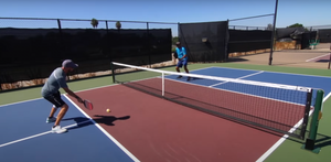 Two players practicing pickleball on a court with a net.