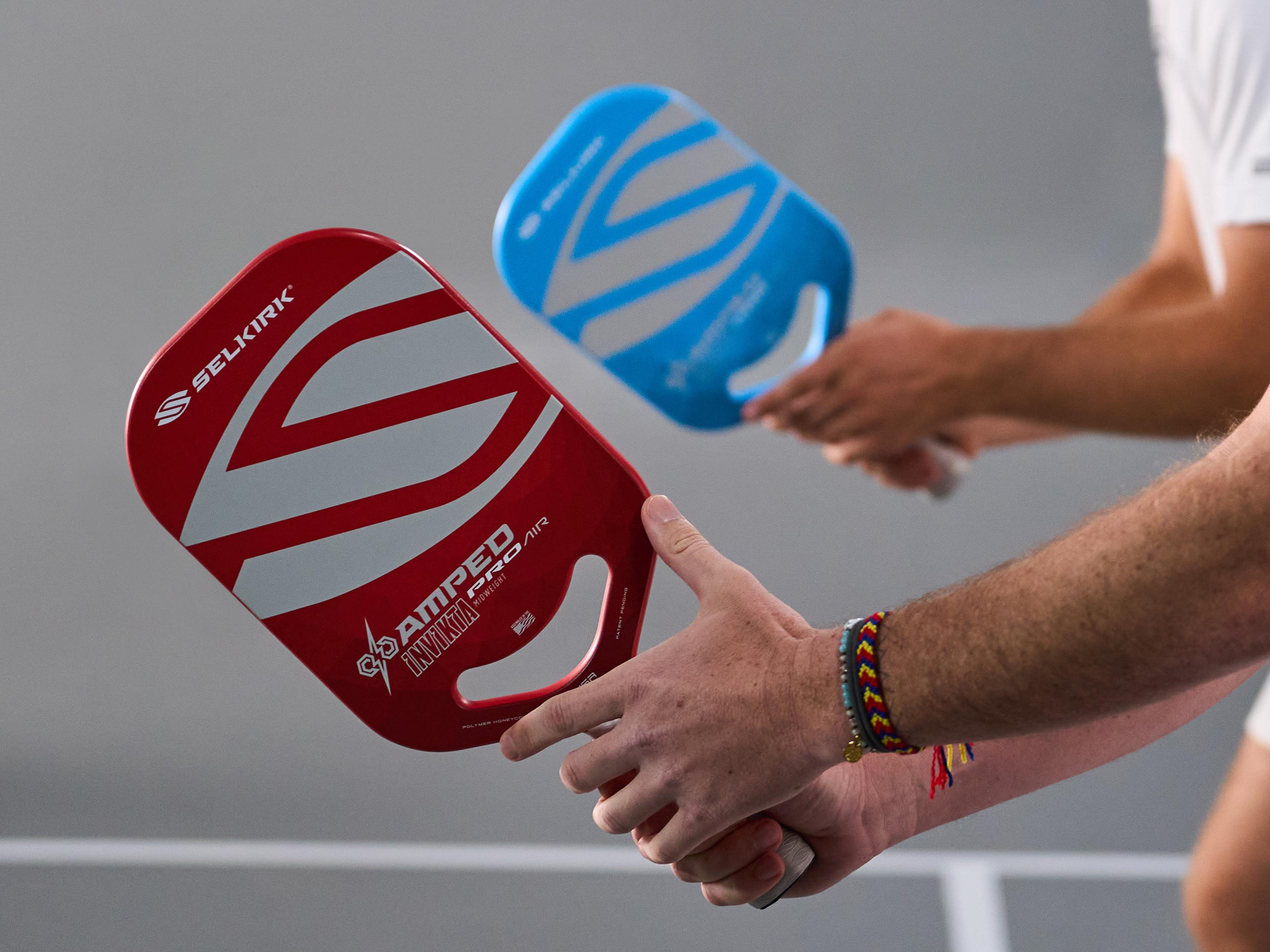 Two pickleball paddles, one red and one blue, being held by players.