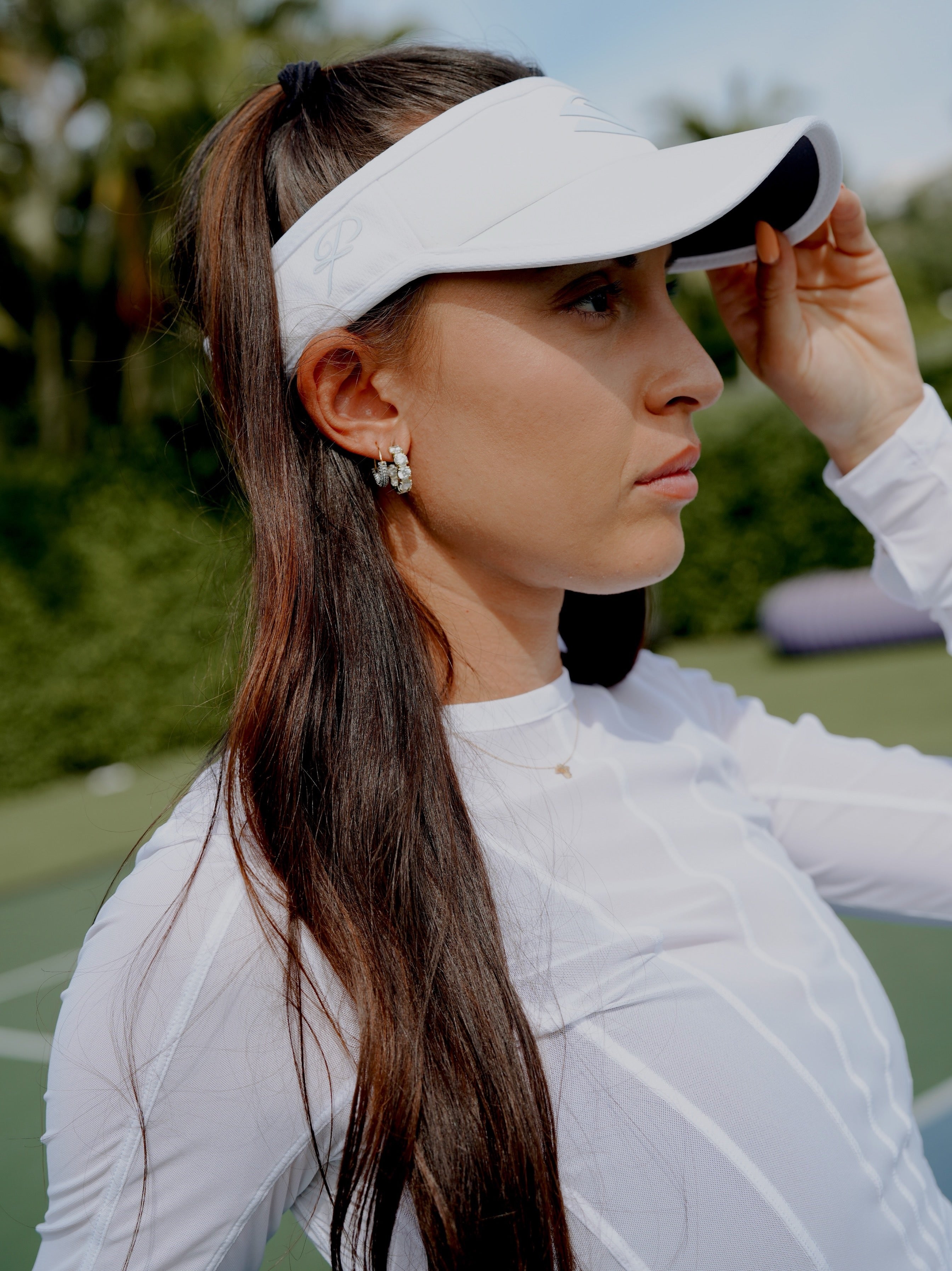 A woman wearing a visor and long hair styled in a high ponytail on a pickleball court