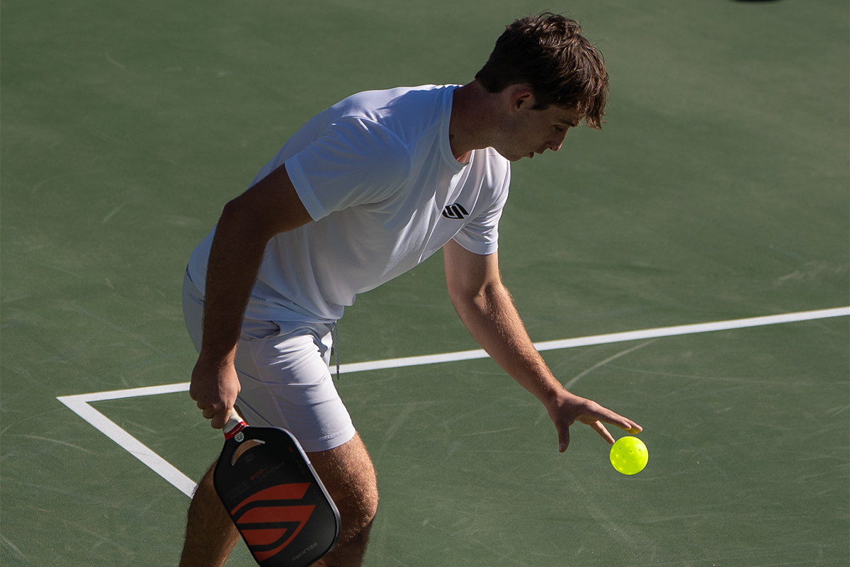 A male pickleball player preparing to serve a yellow ball on a court.