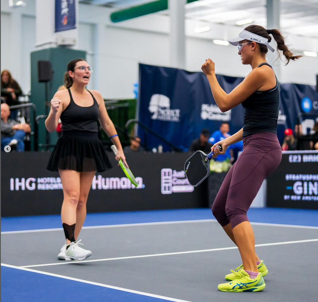 Two female pickleball players celebrating on the court during a match.
