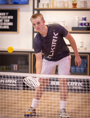 Pickleball player holding a paddle near the net on an indoor court