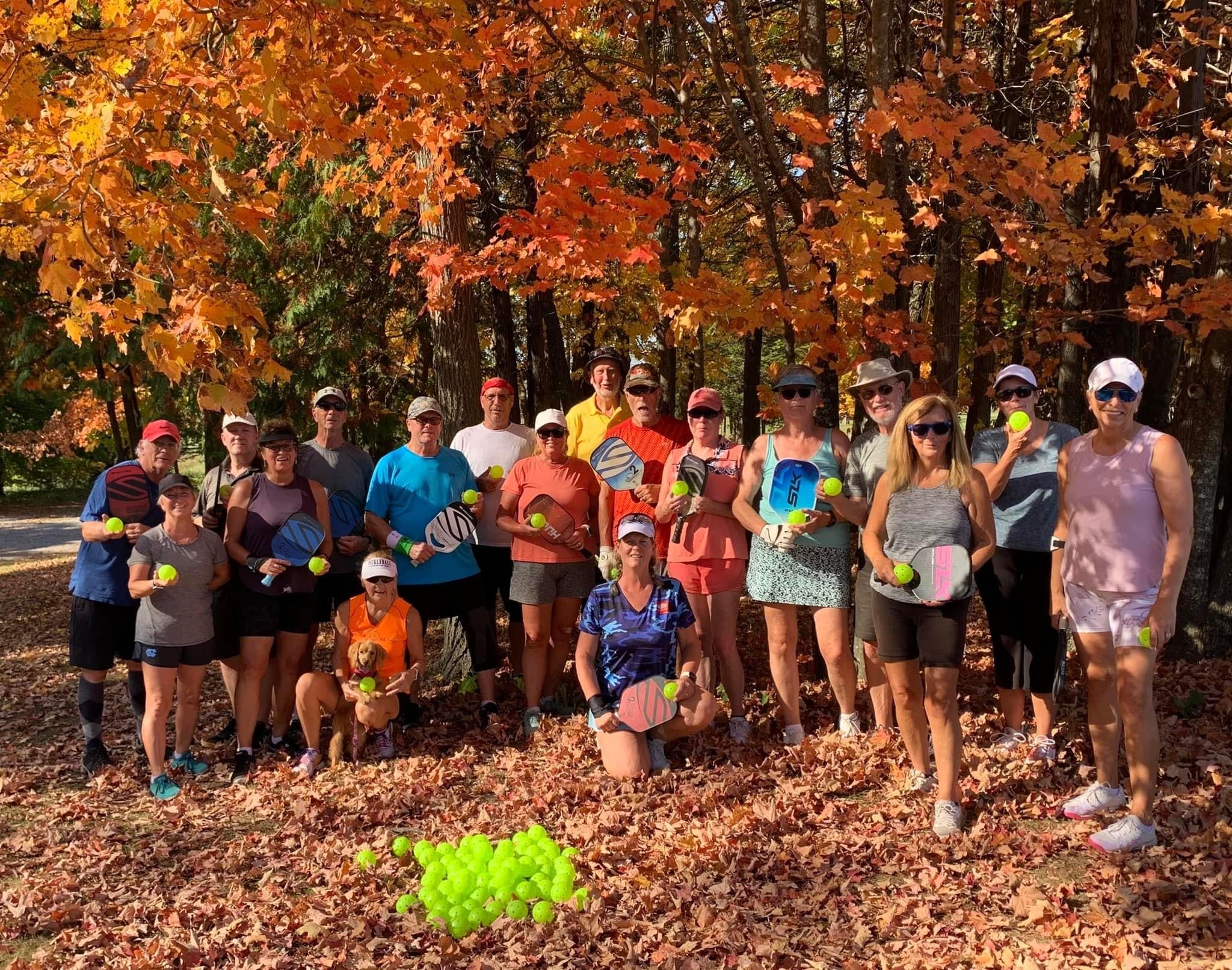 Group of pickleball players holding paddles and balls in a fall setting