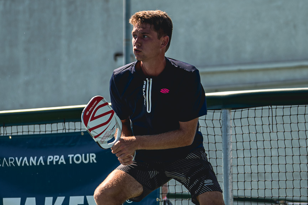 A male player in a blue shirt holding a pickleball paddle, preparing to hit a shot on a court.