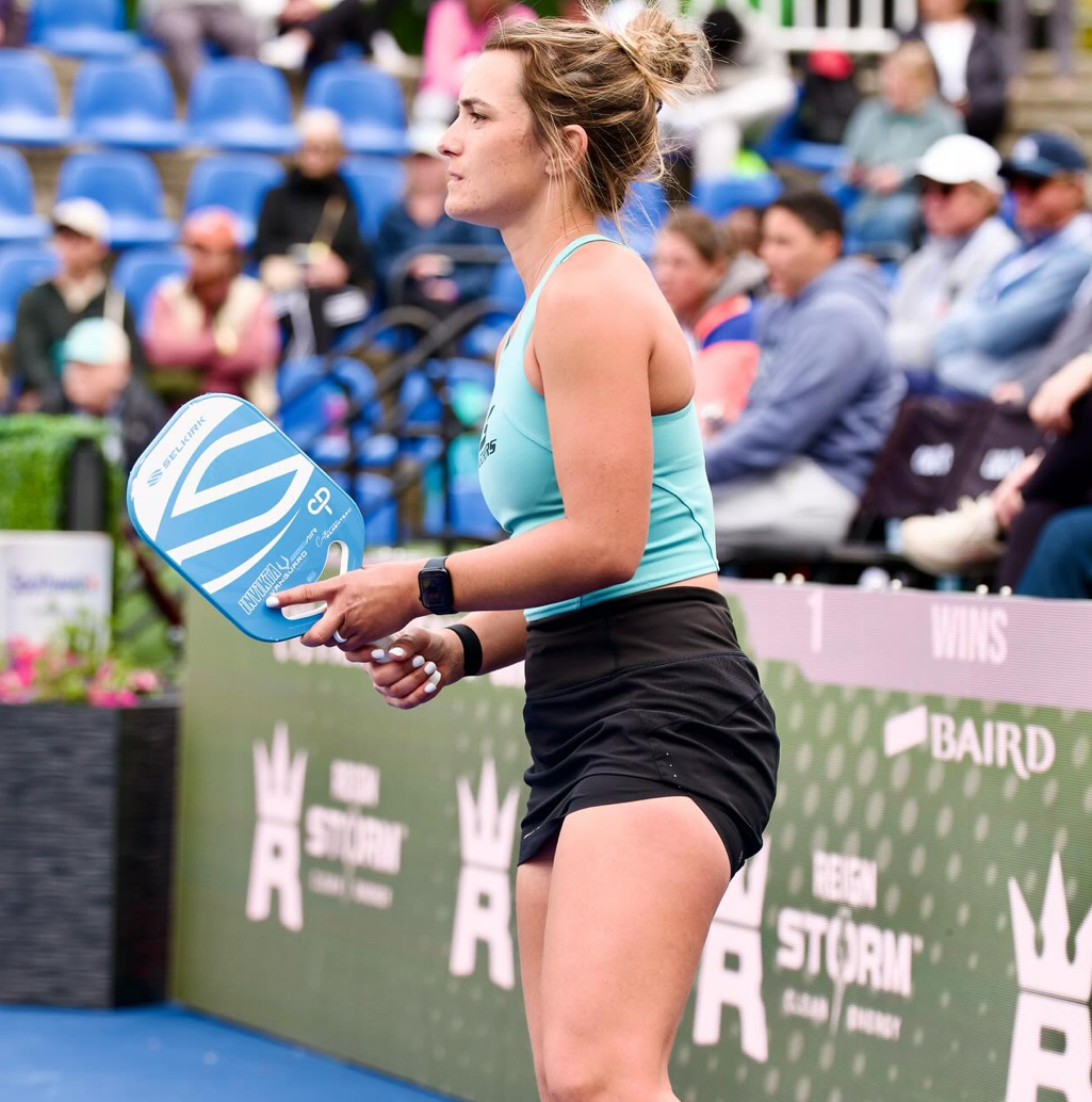 Catherine Parenteau preparing to serve in a pickleball match, with spectators in the background.