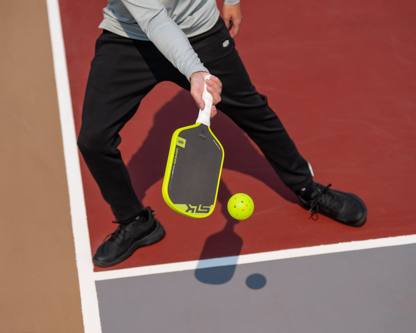 Pickleball player executing a drop shot with a neon yellow SLK paddle while lunging on a red court