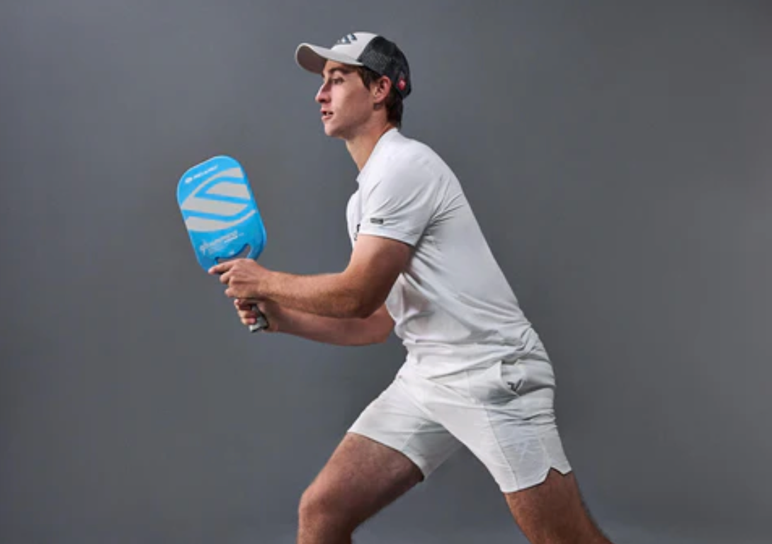 Male pickleball player in white attire preparing to hit a shot with a blue paddle.