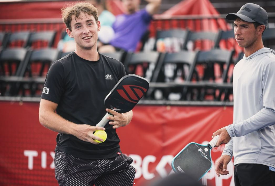 Two pickleball players, one smiling and holding a paddle and ball, at a tournament.