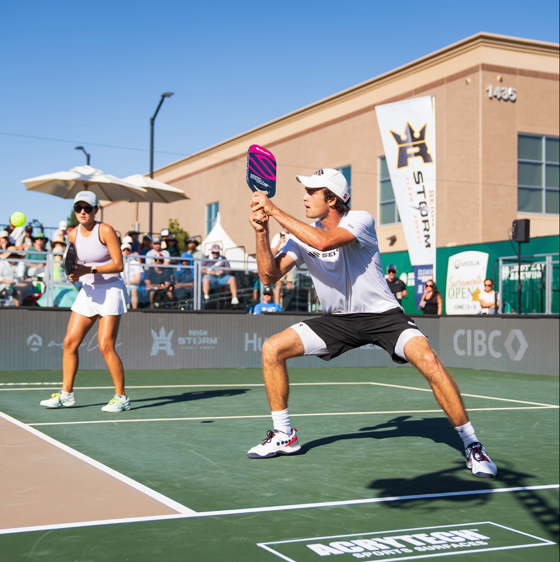 James Ignatowich prepares to hit a shot while Anna Bright stands ready on the court during a pickleball match.