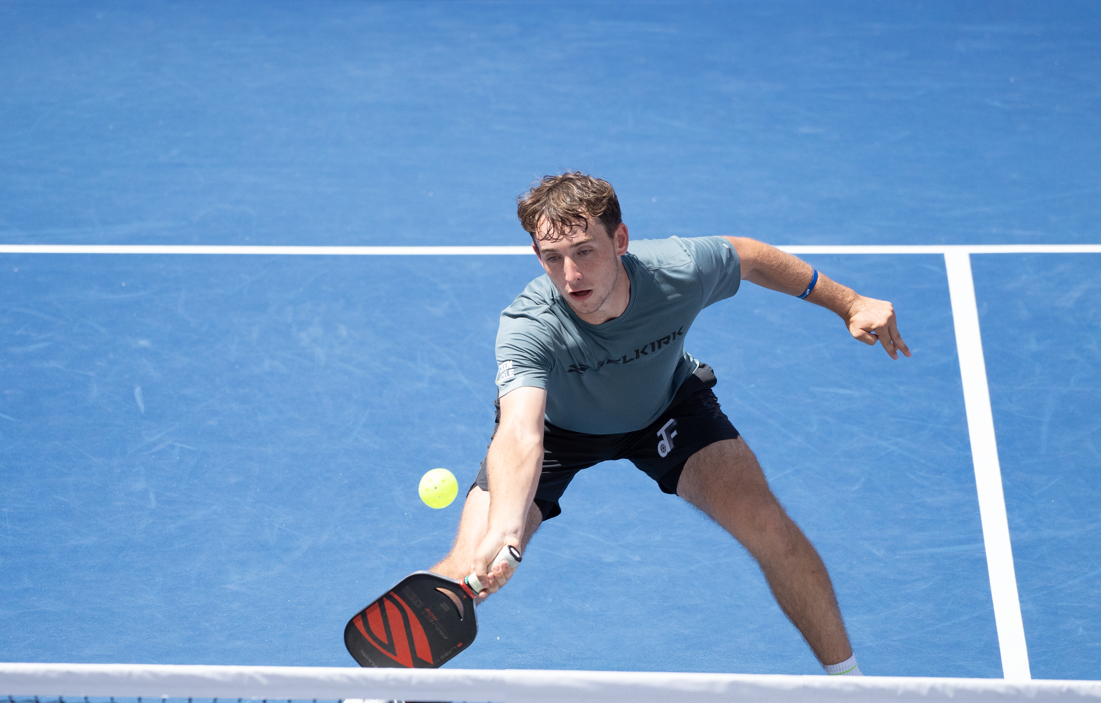 Dylan Frazier lunging to hit a pickleball during a match on a blue court