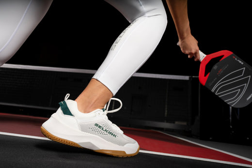 A player preparing to serve in pickleball, wearing white shoes designed for the sport.