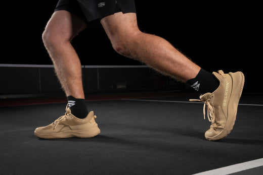 A person wearing beige pickleball shoes on a court surface.