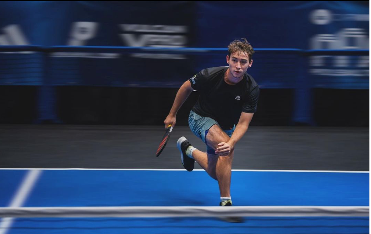Male pickleball player lunging to hit a shot on an indoor blue court during a match