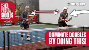 An older man and a younger man play pickleball on an indoor court, with arrows indicating movement and the text 'DOMINATE DOUBLES BY DOING THIS!' in the foreground.