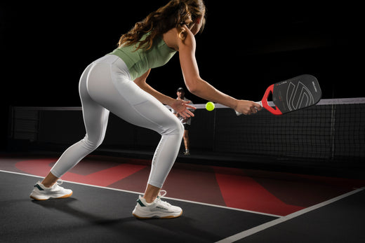 A woman preparing to hit a pickleball with a paddle on a court.