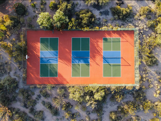 Aerial view of three pickleball courts with green and blue surfaces in a desert setting.