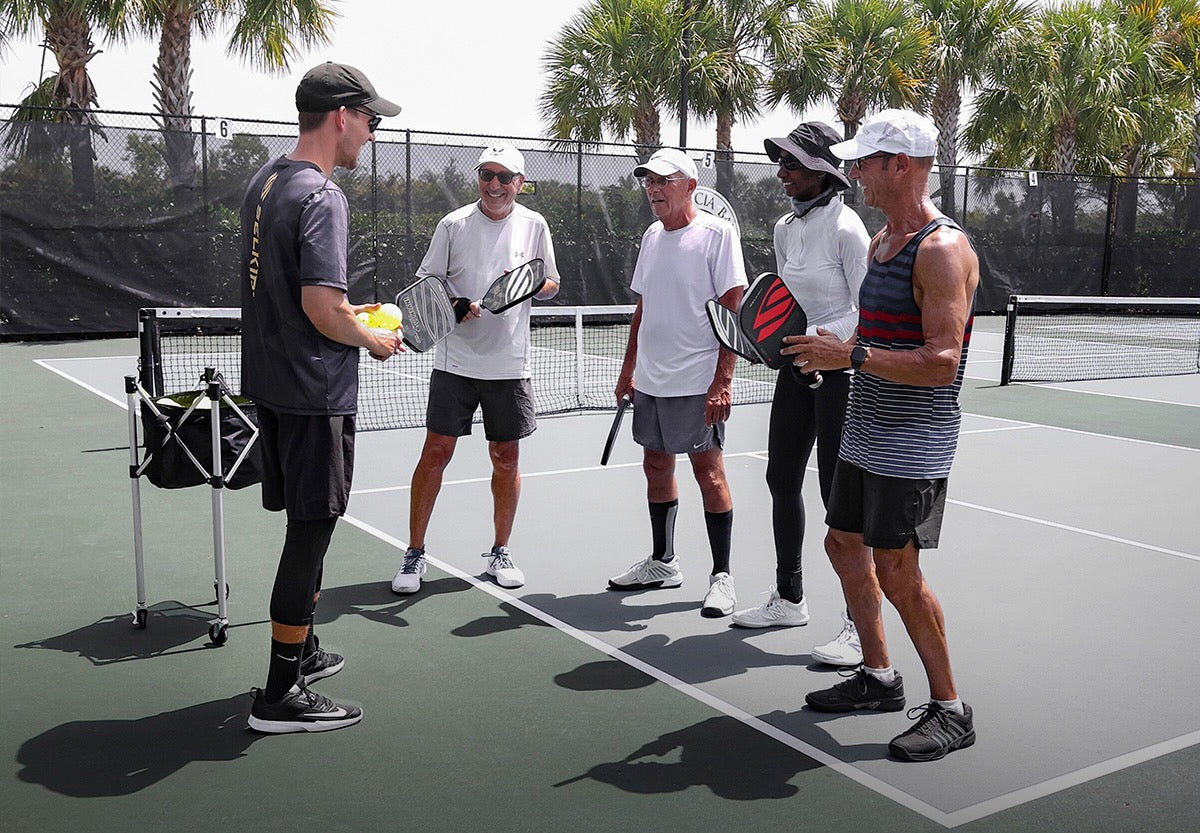 Five people on a pickleball court discussing and holding paddles