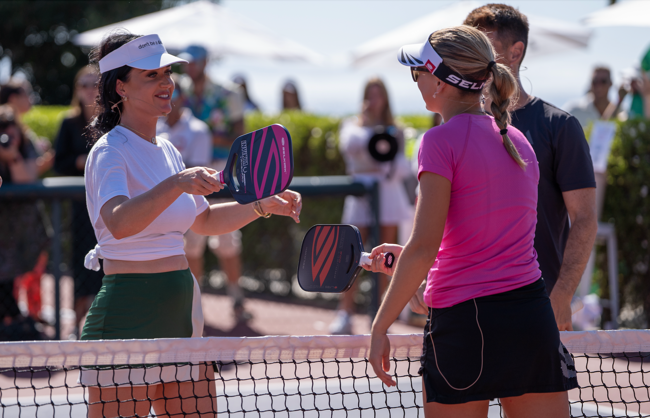 Two players tapping paddles over a pickleball net on an outdoor court.