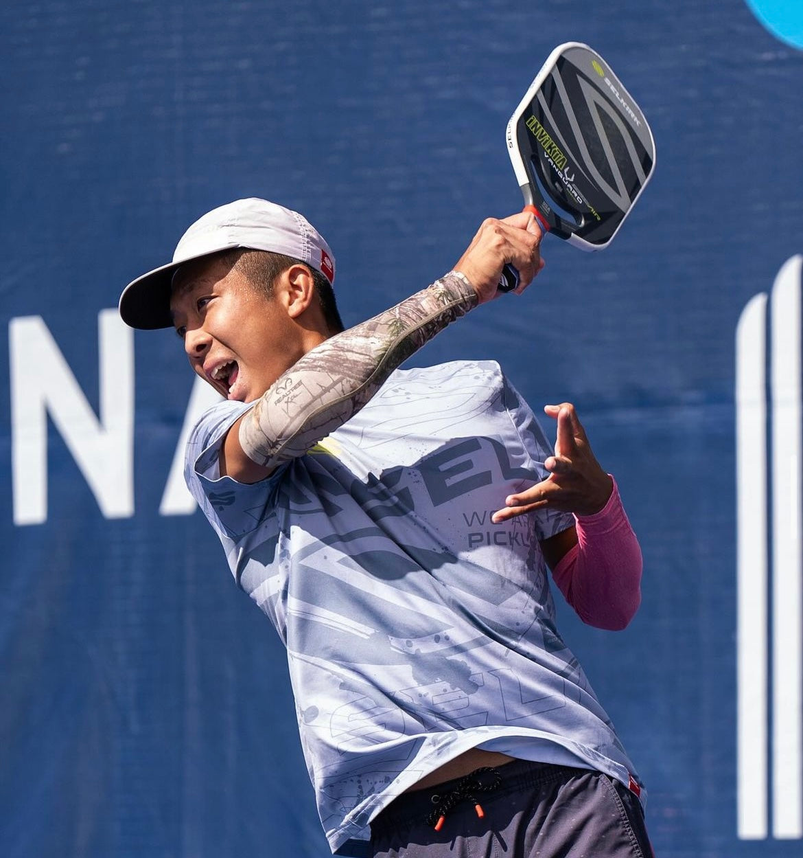 A player in a gray shirt and cap hitting a pickleball with a paddle.