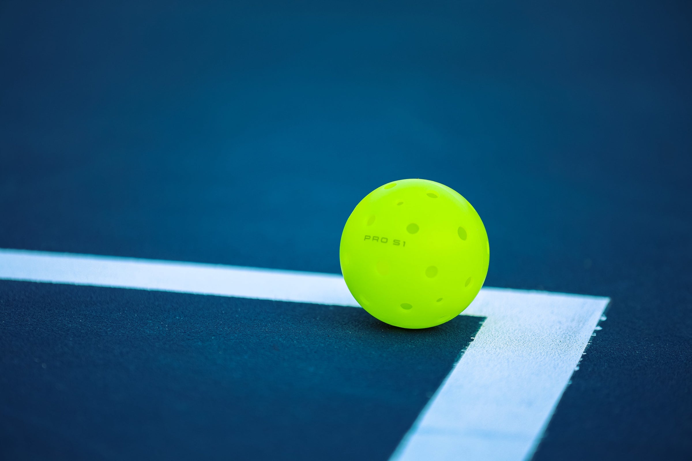 A yellow pickleball resting on the court's boundary line.